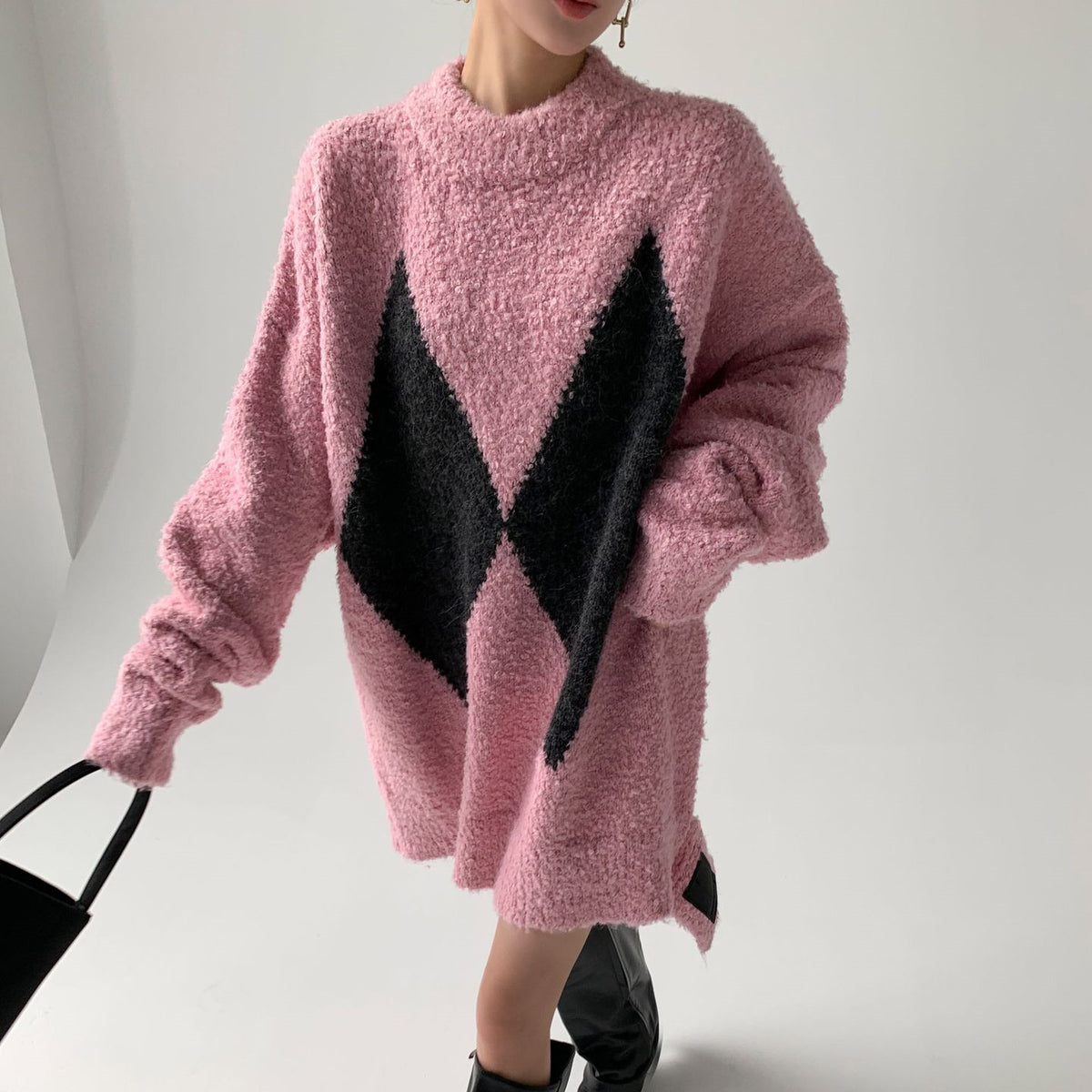 A woman wearing a pink color-blocking diamond pattern wool long sweater shirt with black color accents.