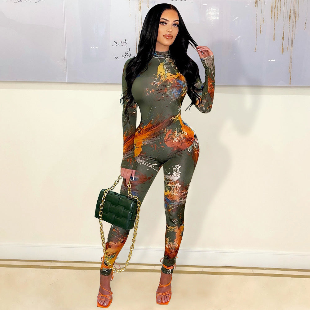 A model wearing a long-sleeved, tight-fitting green jumpsuit with a floral and abstract paint splatter design, featuring a cutout back.